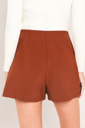 A model wearing a rust-brown wrap-style mini skort with a gold embellishment on the front | Flying Tomato
