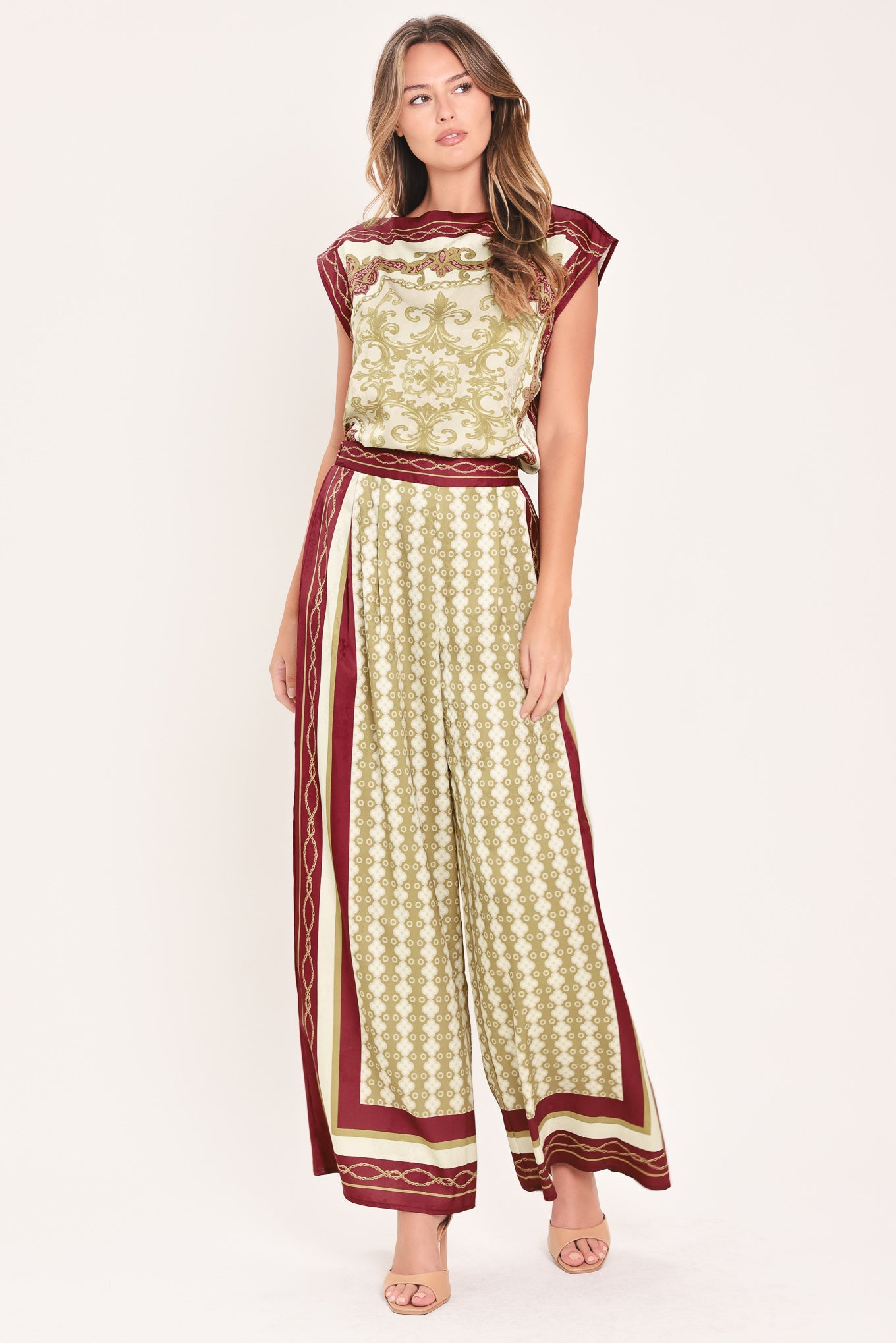 A woman wearing a pair of wide-leg pants with a beige and gold geometric pattern, featuring deep burgundy side panels and a matching patterned hem | Flying Tomato