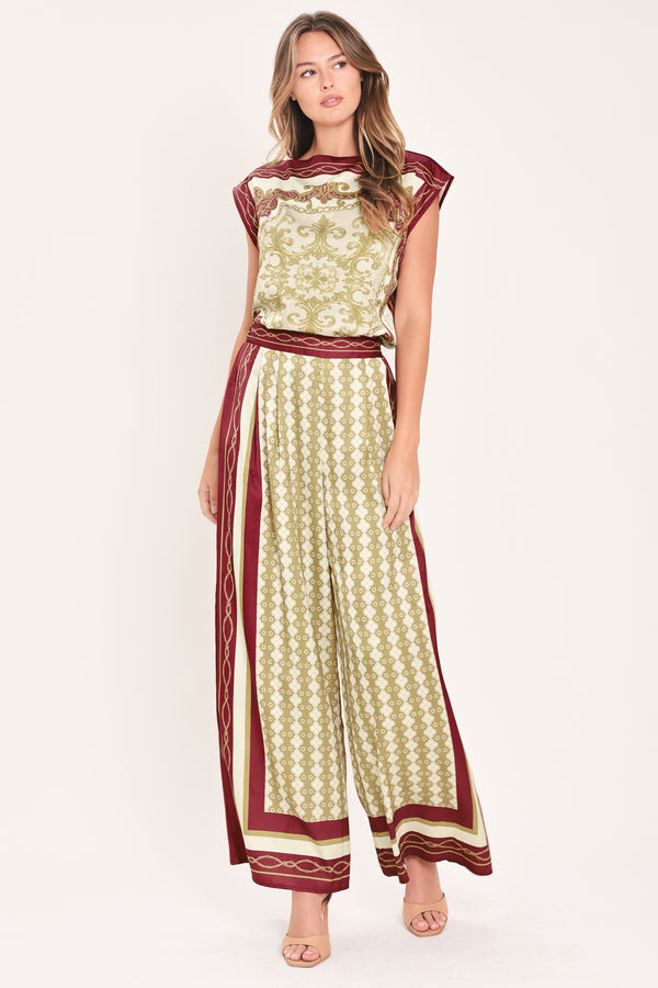 A woman wearing a pair of wide-leg pants with a beige and gold geometric pattern, featuring deep burgundy side panels and a matching patterned hem | Flying Tomato
