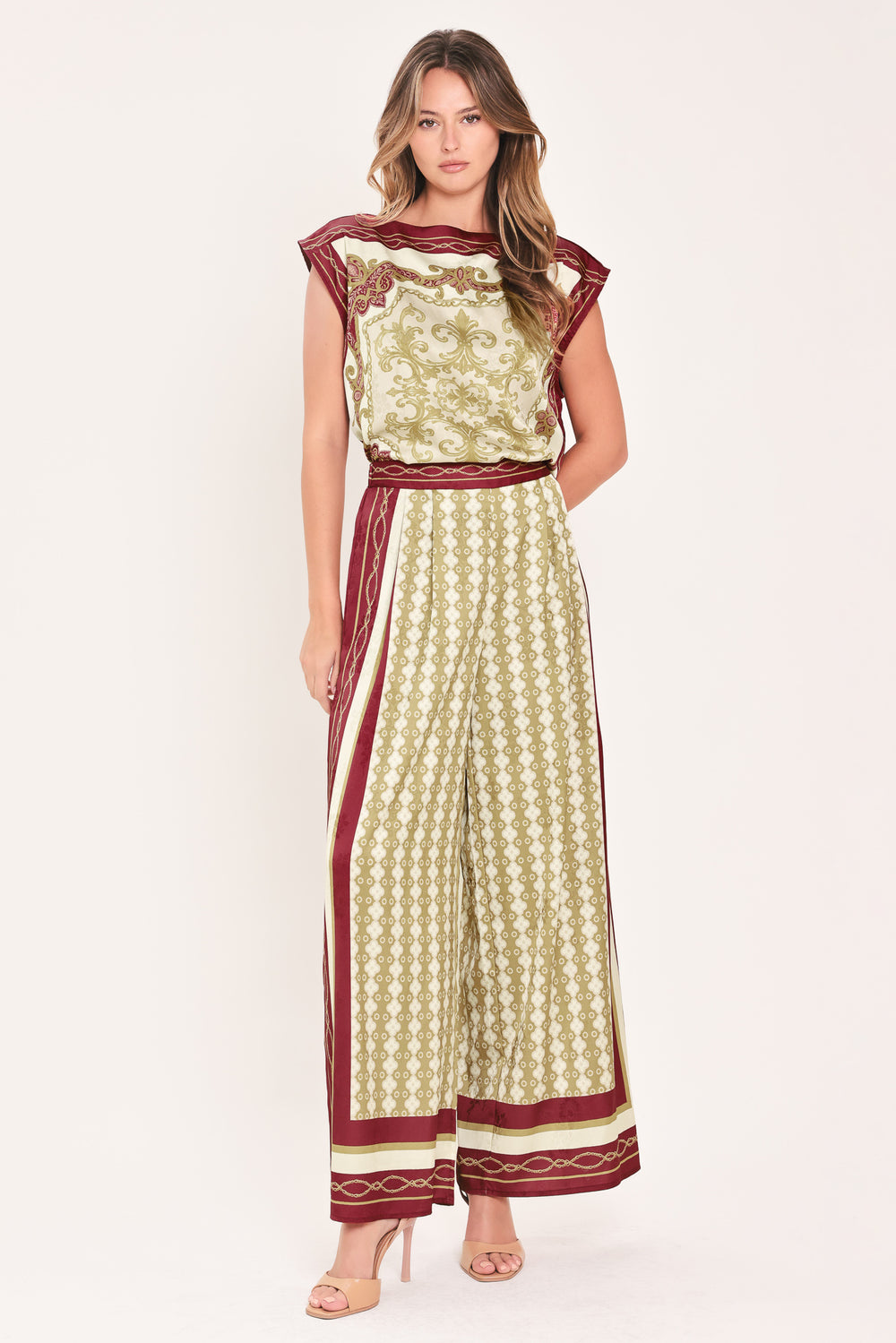 A woman wearing a pair of wide-leg pants with a beige and gold geometric pattern, featuring deep burgundy side panels and a matching patterned hem | Flying Tomato