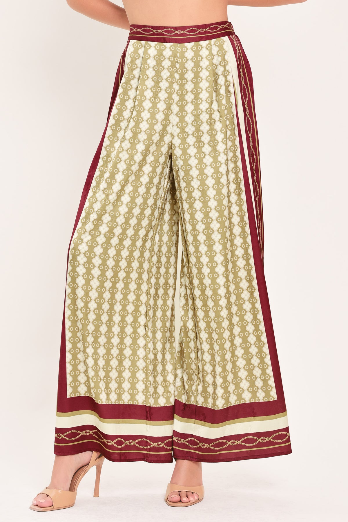 A woman wearing a pair of wide-leg pants with a beige and gold geometric pattern, featuring deep burgundy side panels and a matching patterned hem | Flying Tomato