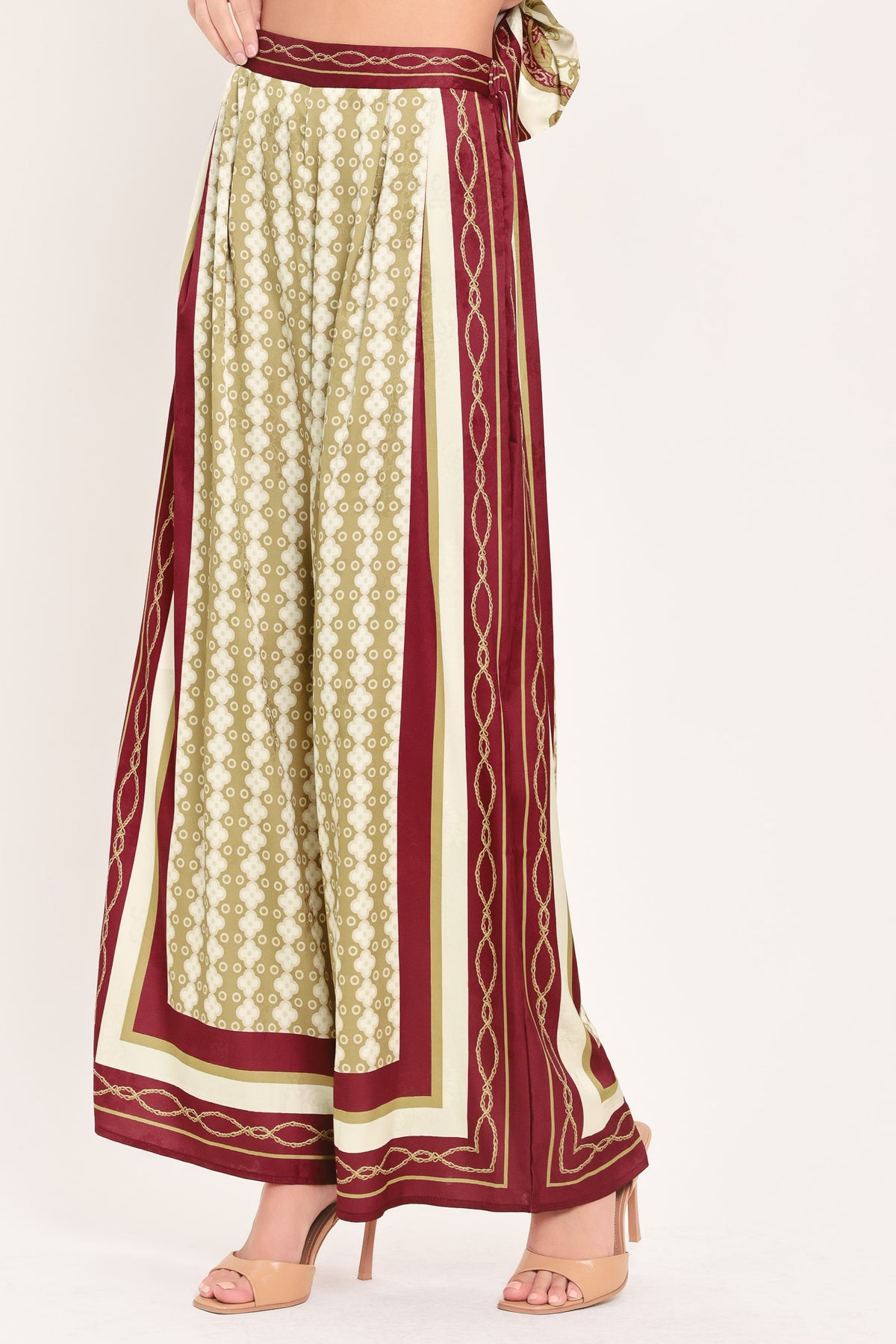 A woman wearing a pair of wide-leg pants with a beige and gold geometric pattern, featuring deep burgundy side panels and a matching patterned hem | Flying Tomato