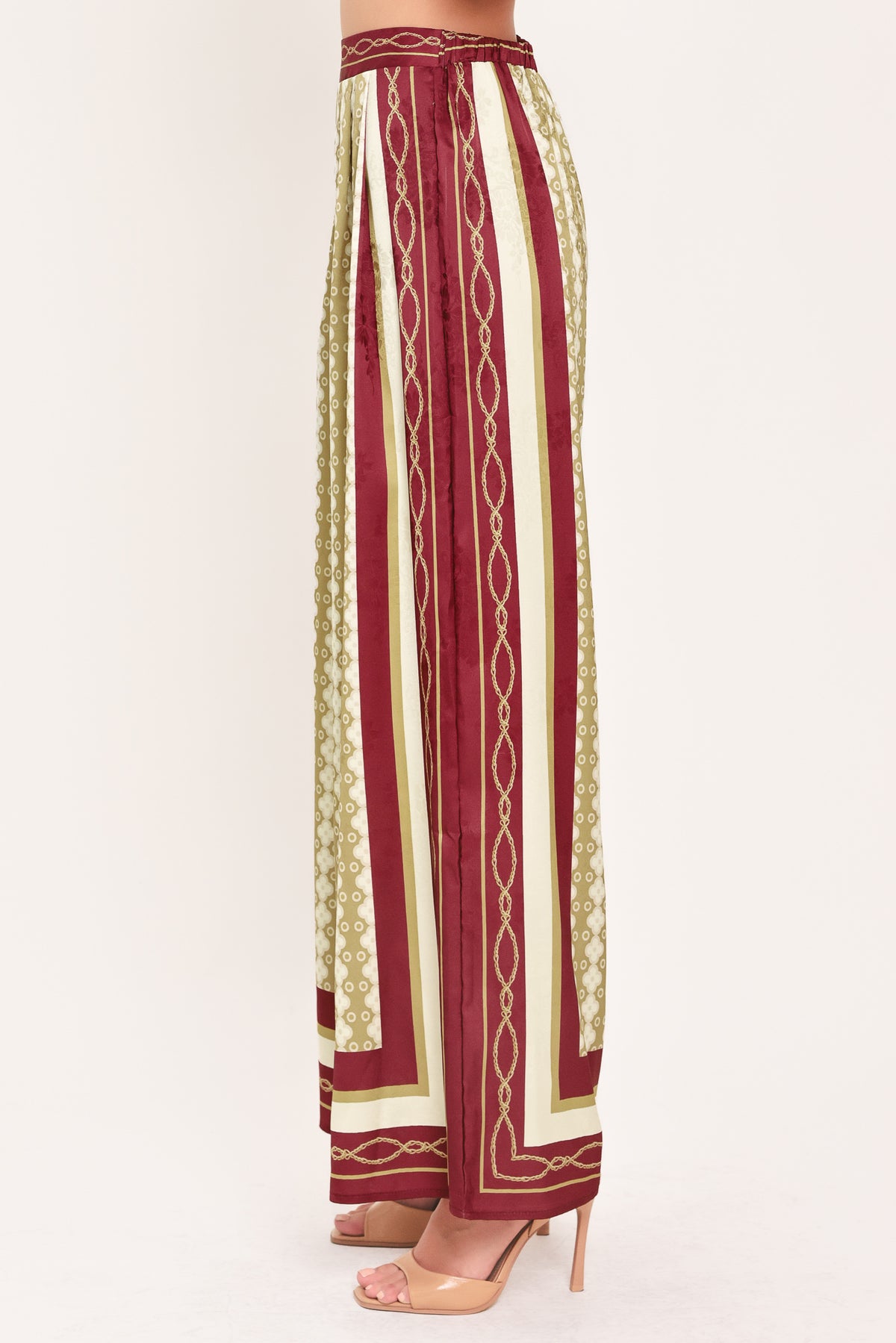A woman wearing a pair of wide-leg pants with a beige and gold geometric pattern, featuring deep burgundy side panels and a matching patterned hem | Flying Tomato