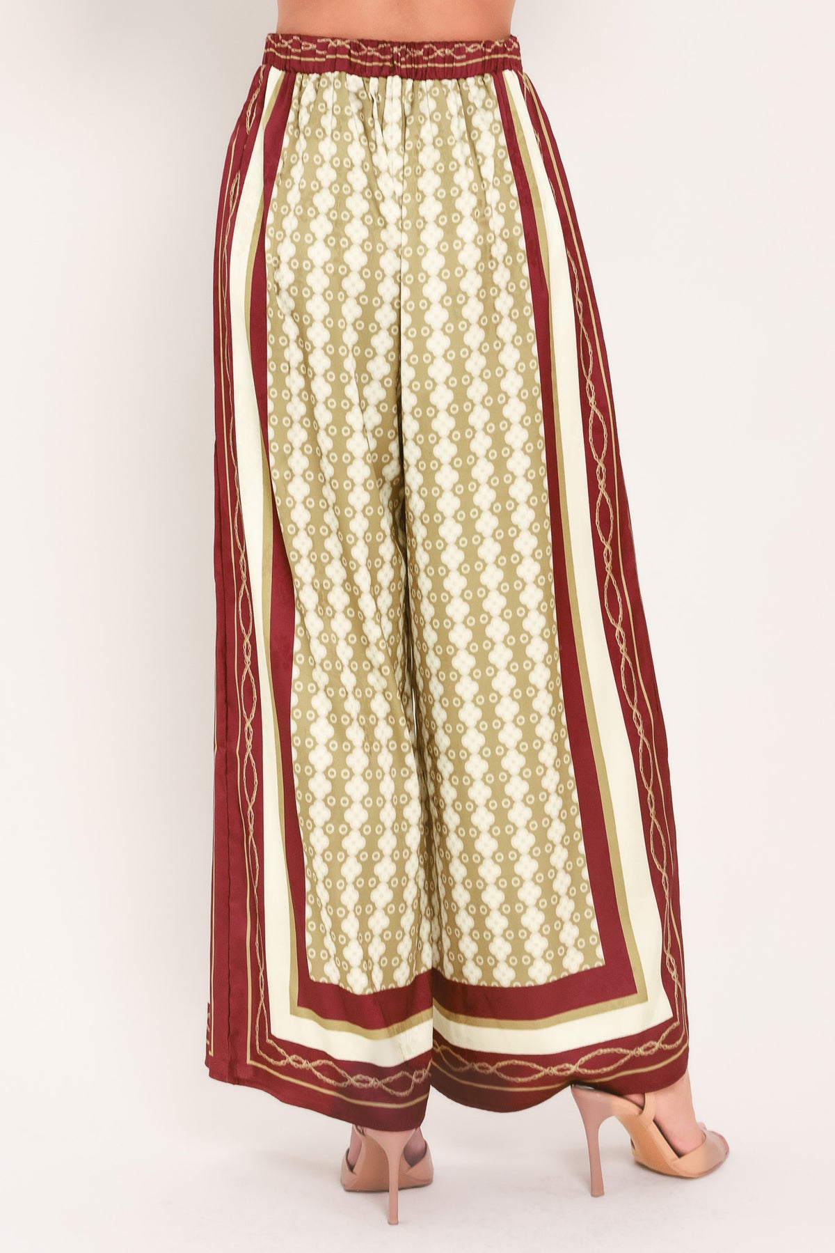 A woman wearing a pair of wide-leg pants with a beige and gold geometric pattern, featuring deep burgundy side panels and a matching patterned hem | Flying Tomato