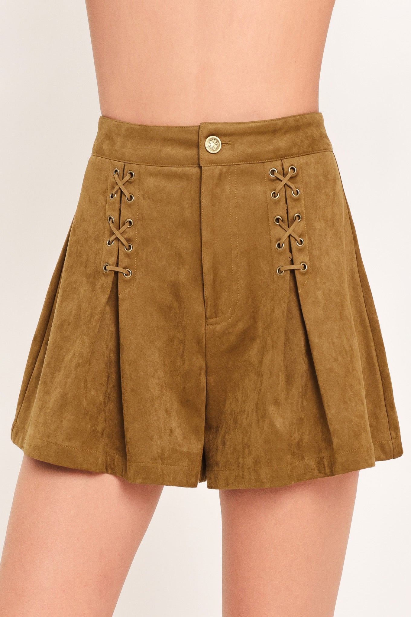 A woman wearing a camel suede mini skort with pleated detailing and lace-up front accents | Flying Tomato