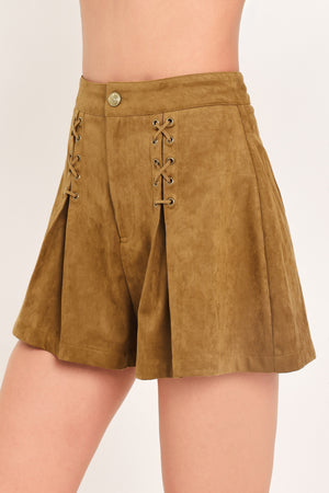 A woman wearing a camel suede mini skort with pleated detailing and lace-up front accents | Flying Tomato