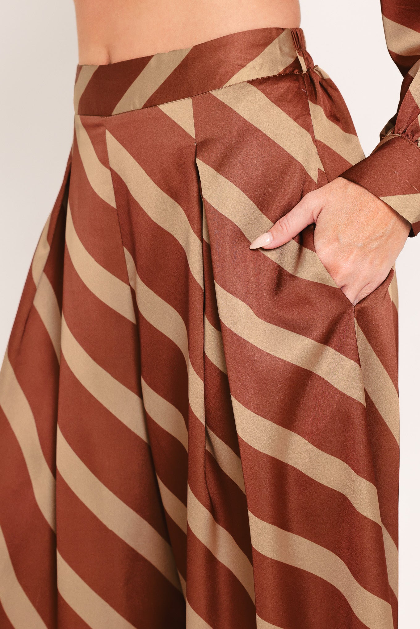 A pair of wide-leg pants with a diagonal striped pattern in rust brown and beige, shown on a model | Flying Tomato