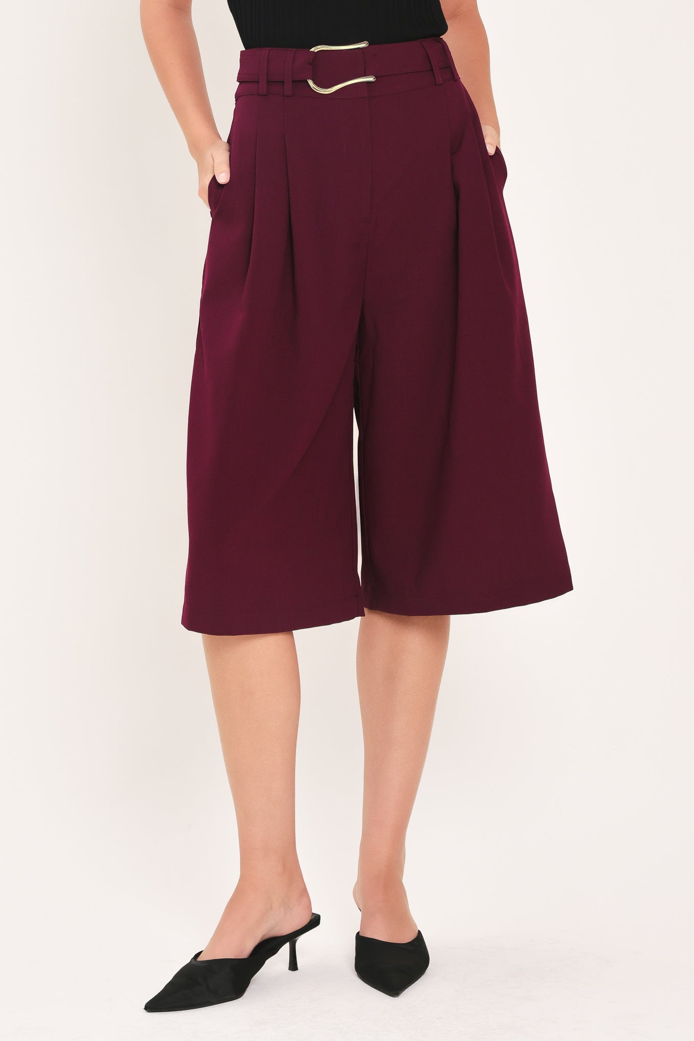 A model wearing high-waisted, wide-leg cropped trousers in deep burgundy with pleats and a matching belt | Flying Tomato
