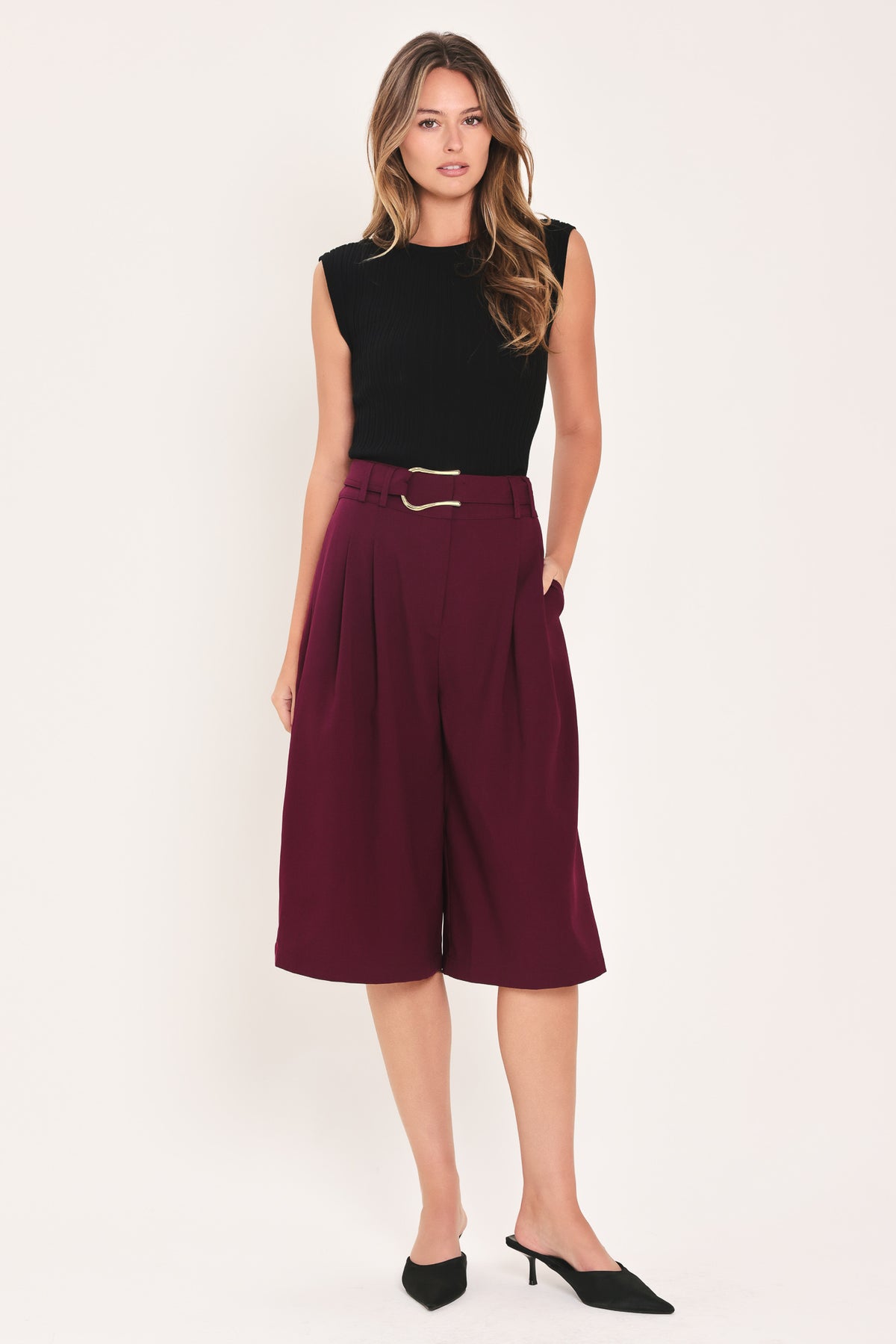 A model wearing high-waisted, wide-leg cropped trousers in deep burgundy with pleats and a matching belt | Flying Tomato