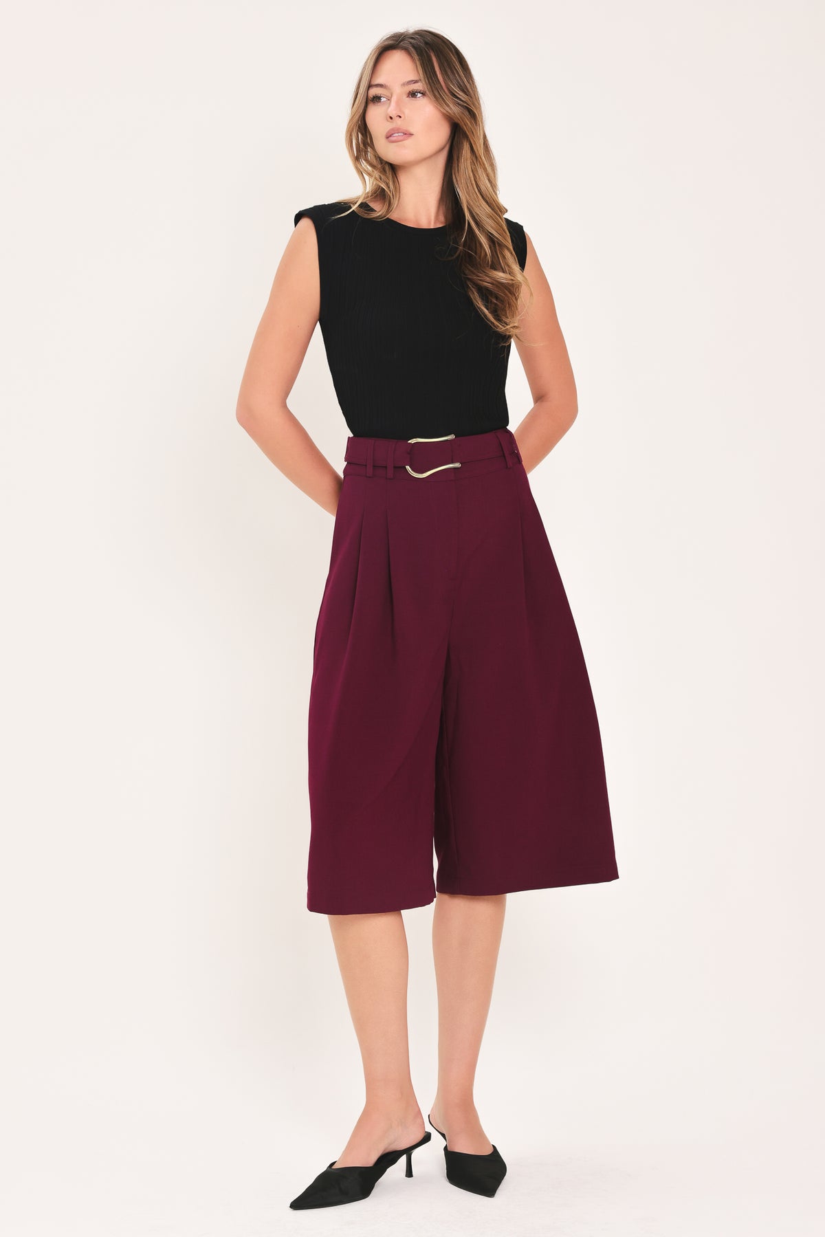 A model wearing high-waisted, wide-leg cropped trousers in deep burgundy with pleats and a matching belt | Flying Tomato
