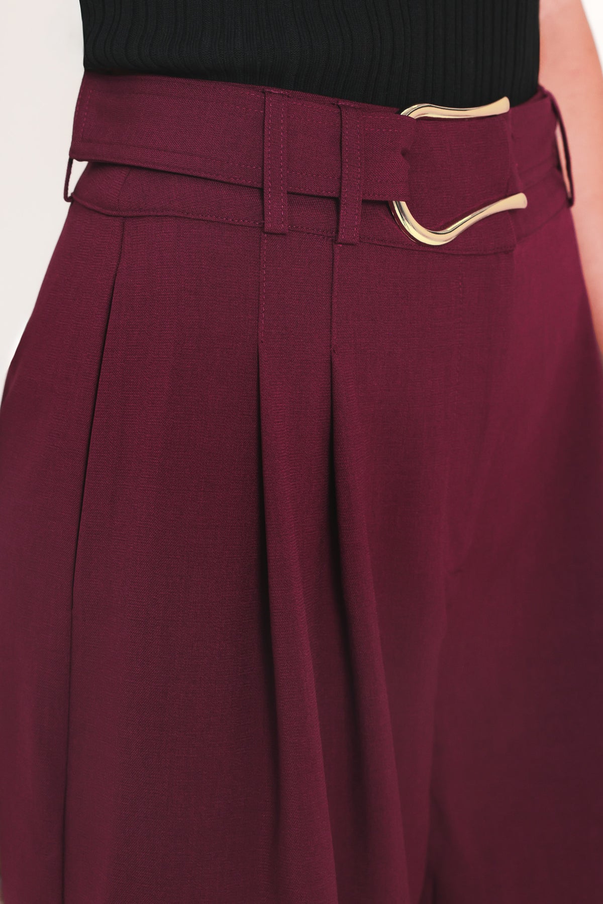 A model wearing high-waisted, wide-leg cropped trousers in deep burgundy with pleats and a matching belt | Flying Tomato