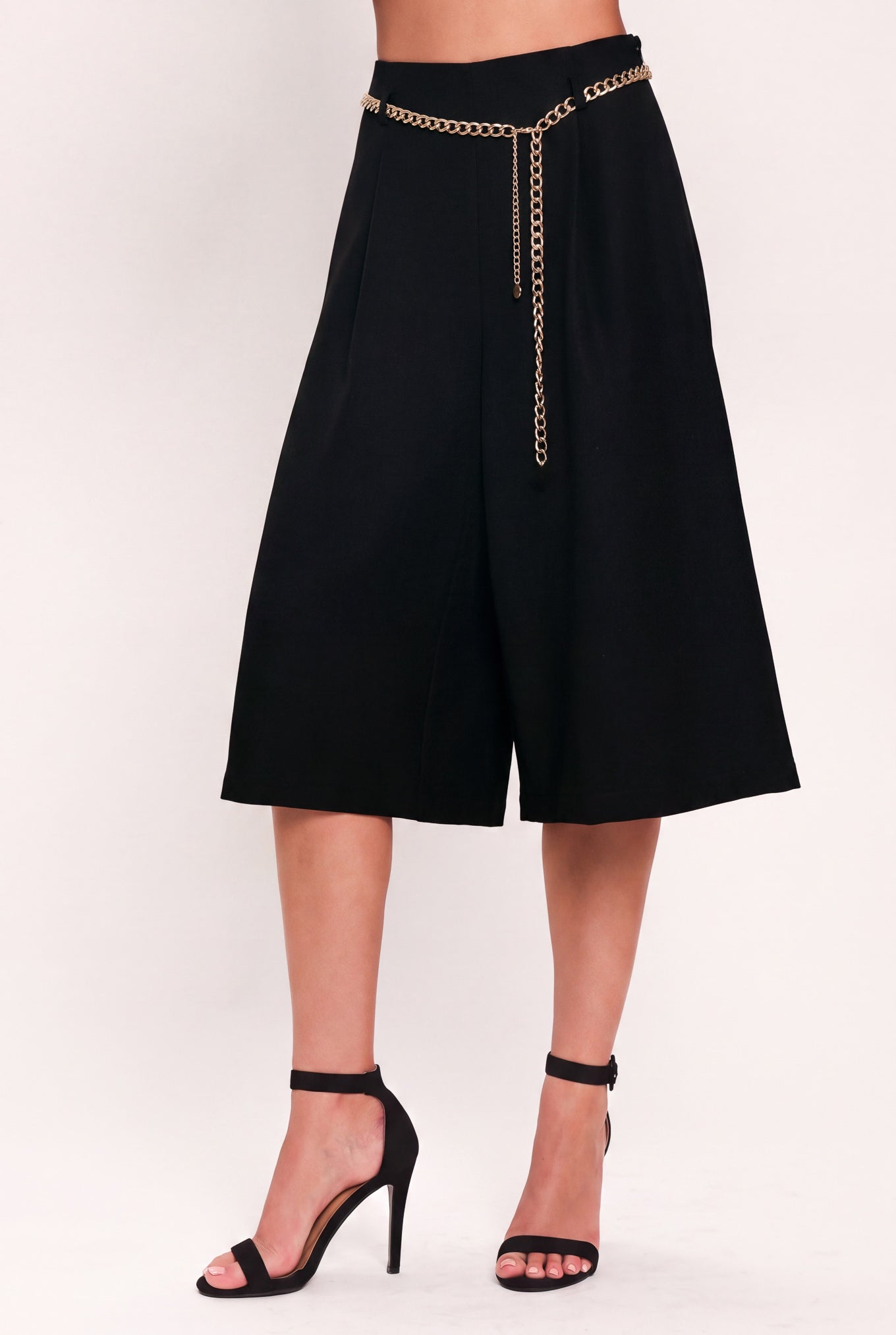 A model wearing a black high-waisted culotta skirt with a gold chain belt detail | Flying Tomato
