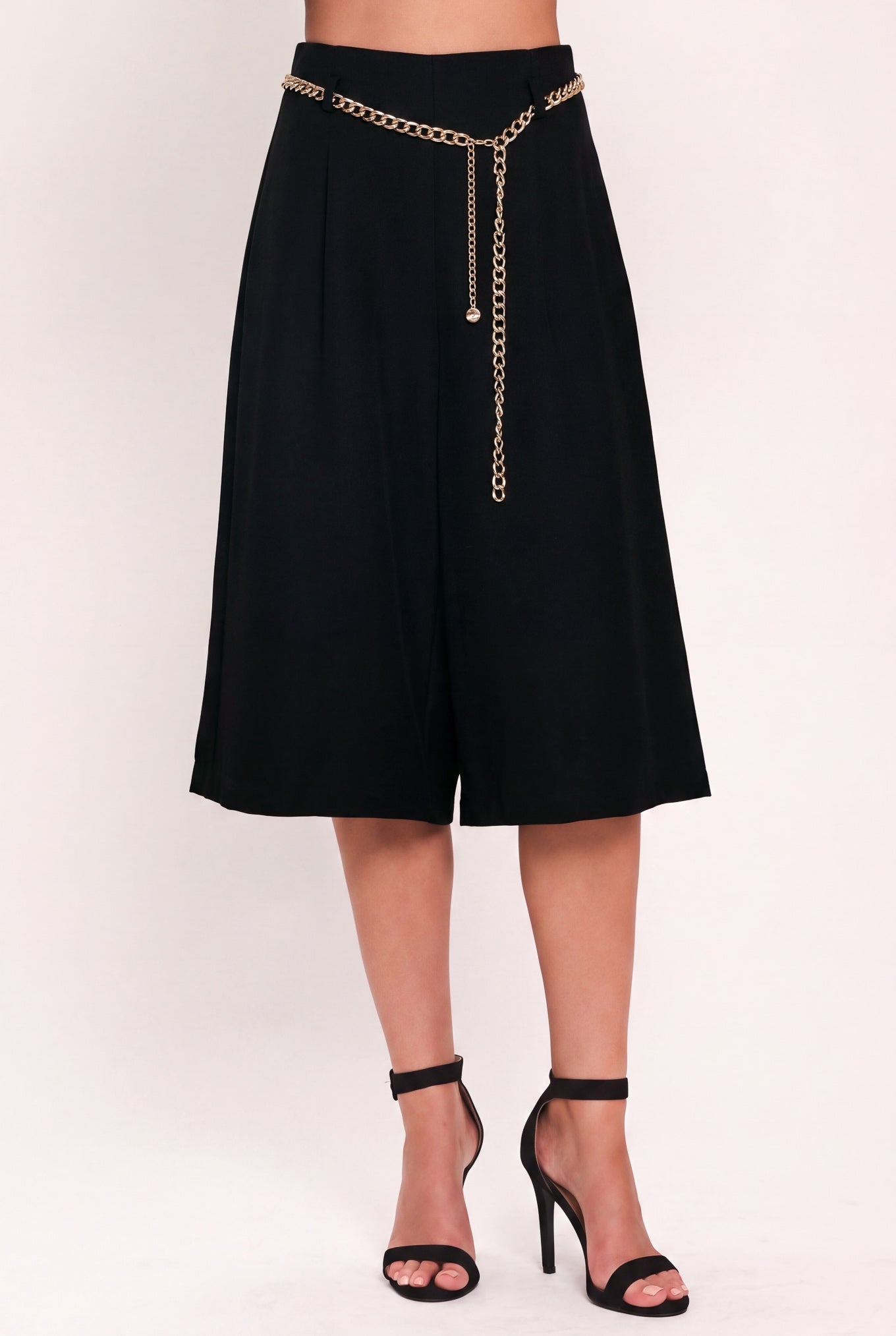 A model wearing a black high-waisted culotta skirt with a gold chain belt detail | Flying Tomato