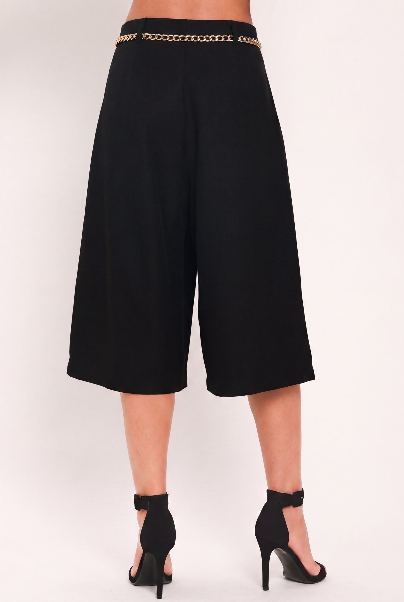 A model wearing a black high-waisted culotta skirt with a gold chain belt detail | Flying Tomato