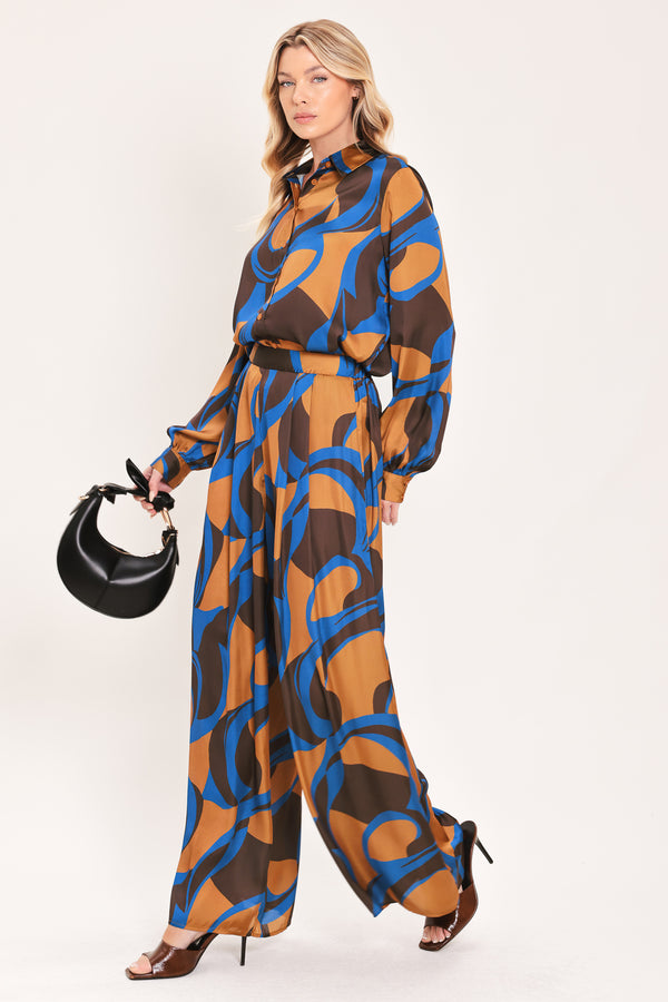 A woman modeling wide-leg pants with a bold abstract swirl pattern in brown, blue, and black | Flying Tomato