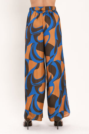 A woman modeling wide-leg pants with a bold abstract swirl pattern in brown, blue, and black | Flying Tomato