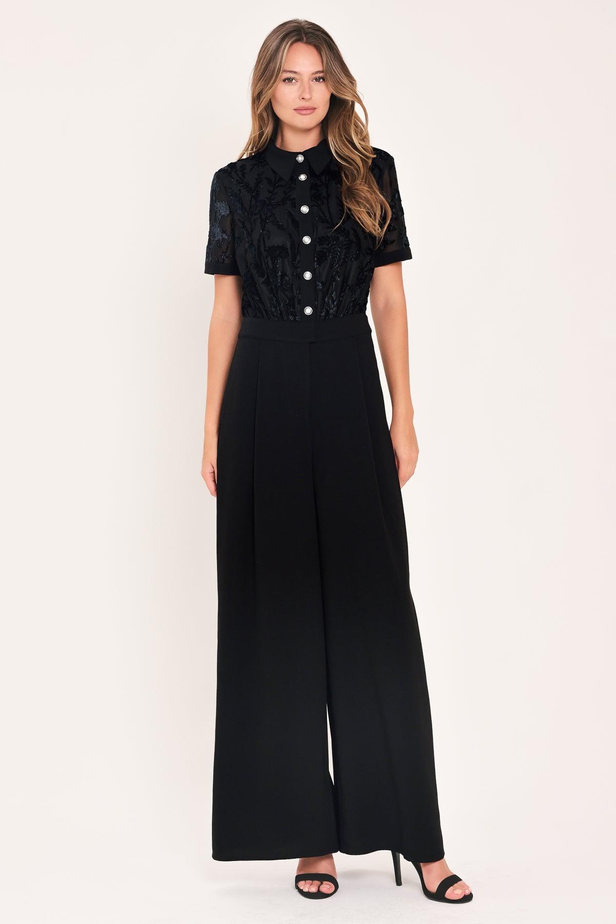 A woman modeling a black short-sleeve jumpsuit with a ruffled button-front bodice and wide-leg pants | Flying Tomato