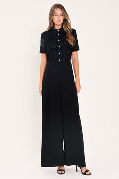 A woman modeling a black short-sleeve jumpsuit with a ruffled button-front bodice and wide-leg pants | Flying Tomato