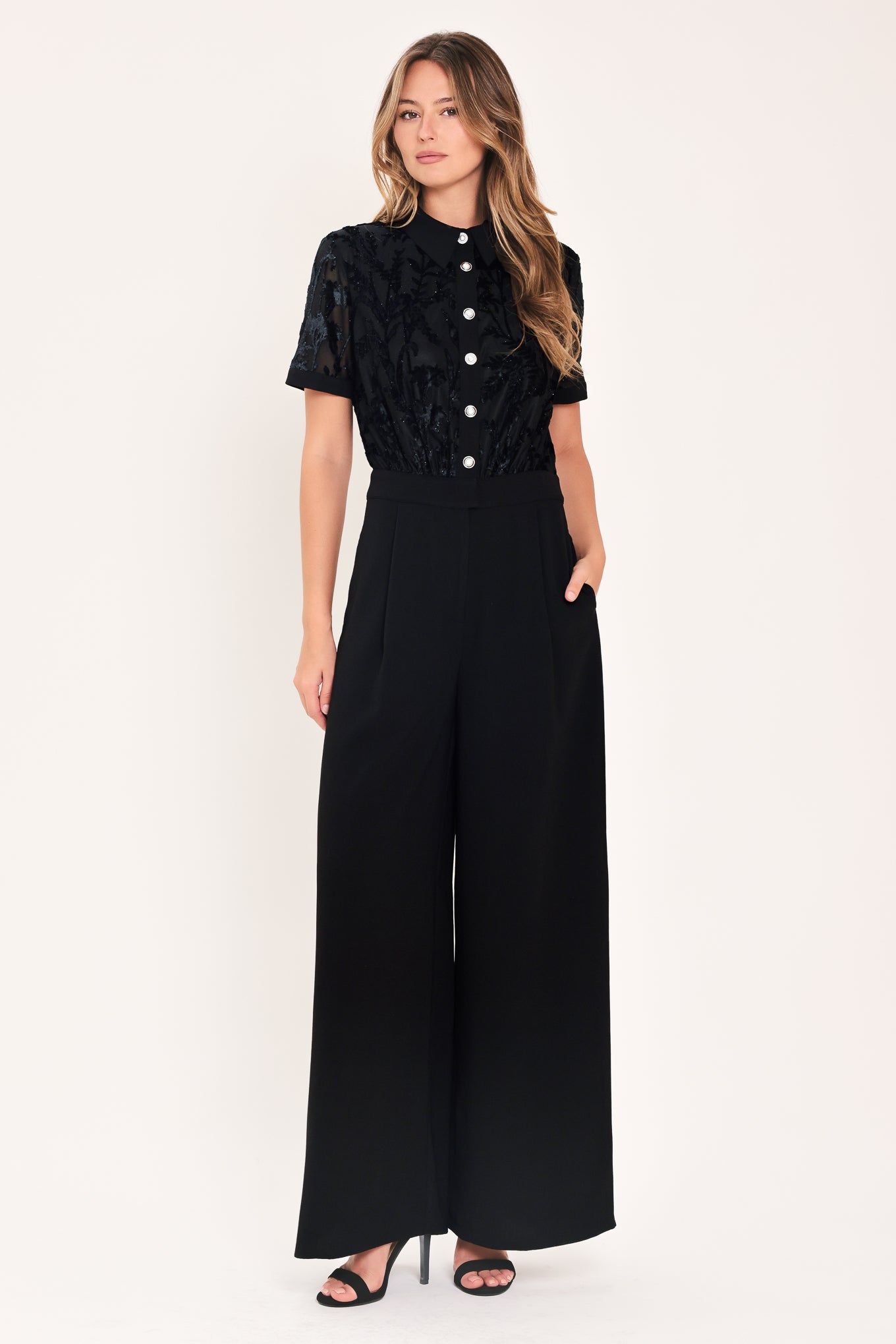 A woman modeling a black short-sleeve jumpsuit with a ruffled button-front bodice and wide-leg pants | Flying Tomato