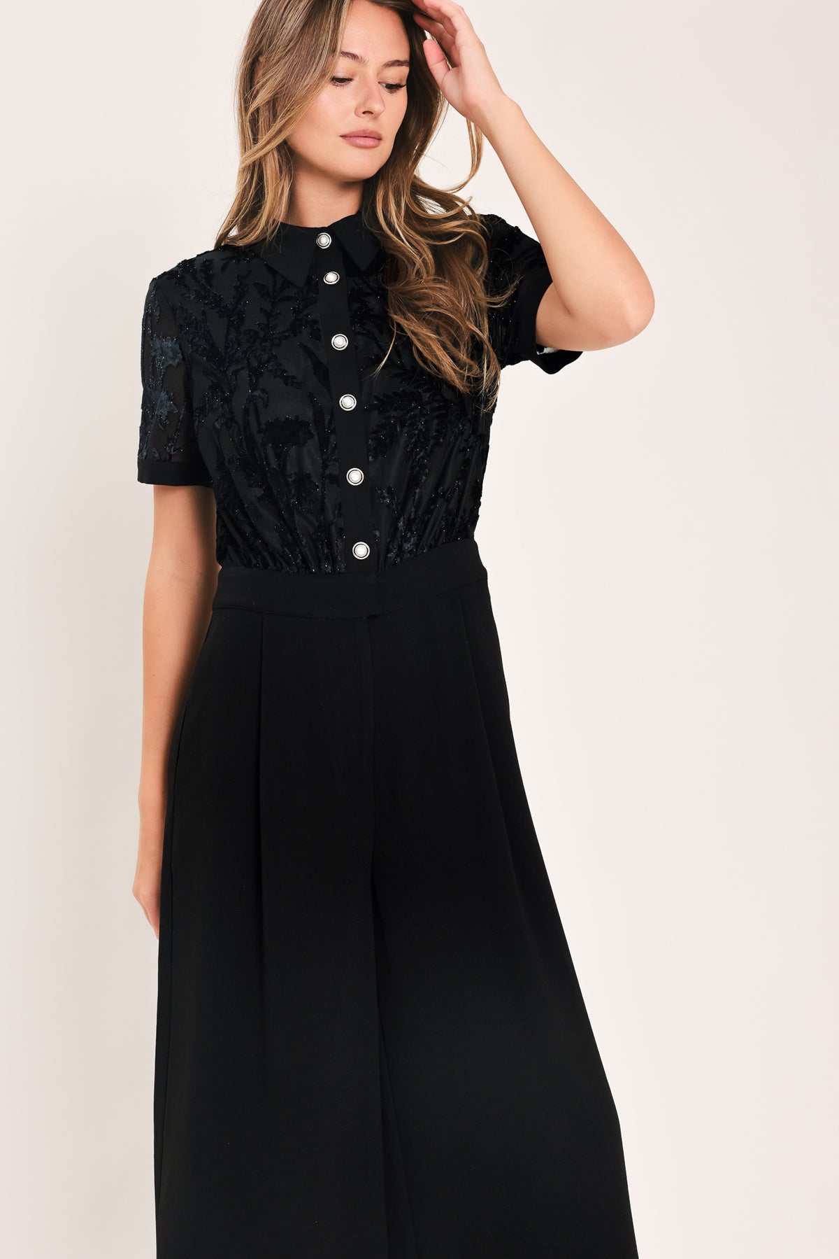 A woman modeling a black short-sleeve jumpsuit with a ruffled button-front bodice and wide-leg pants | Flying Tomato