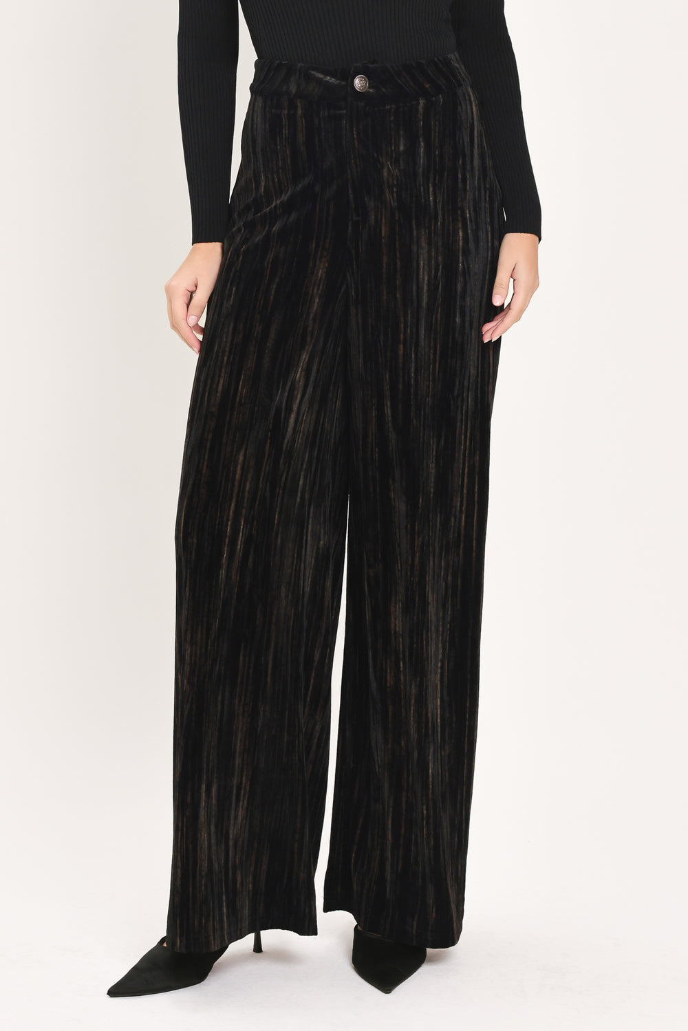 A model wearing high-waisted, wide-leg black pleated velvet trousers with a button waistband | Flying Tomato