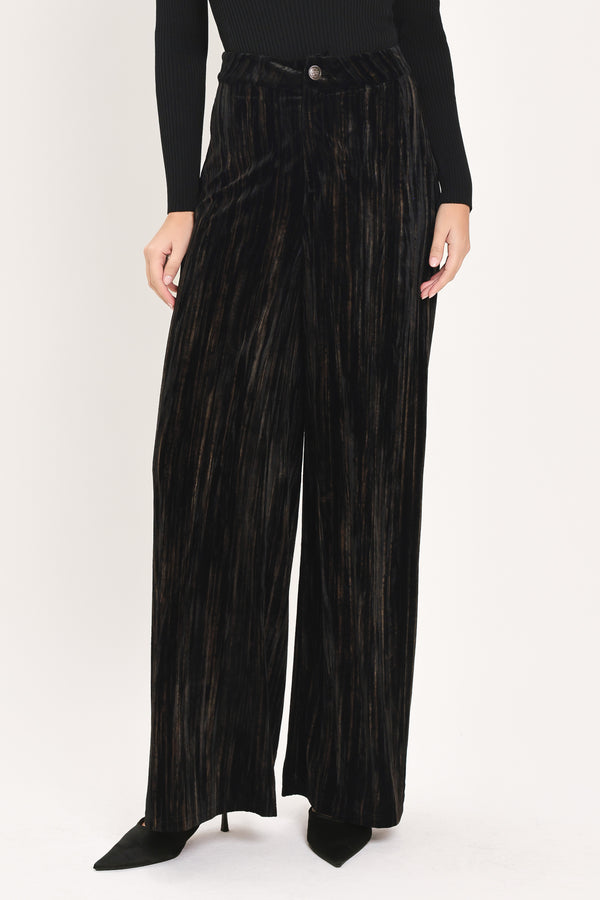 A model wearing high-waisted, wide-leg black pleated velvet trousers with a button waistband | Flying Tomato