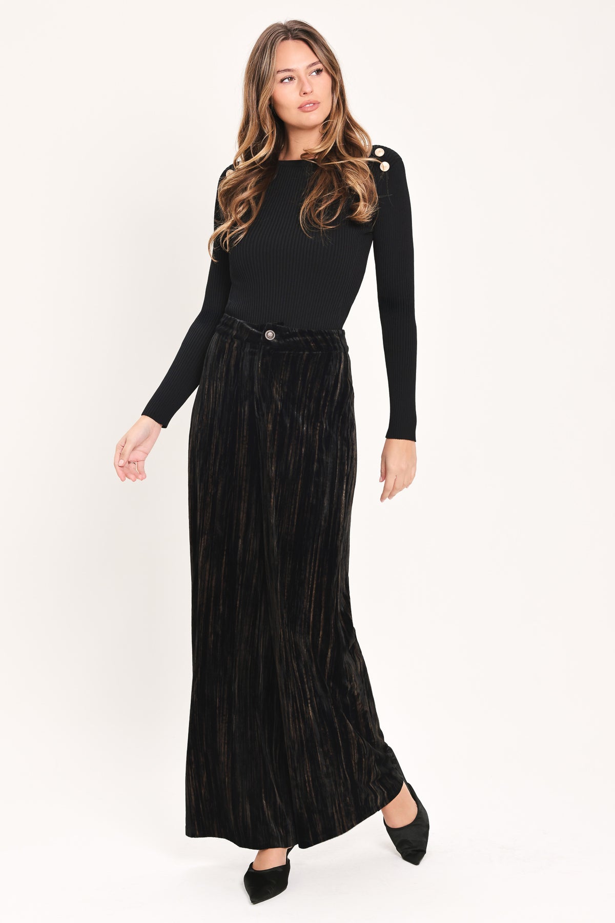 A model wearing high-waisted, wide-leg black pleated velvet trousers with a button waistband | Flying Tomato