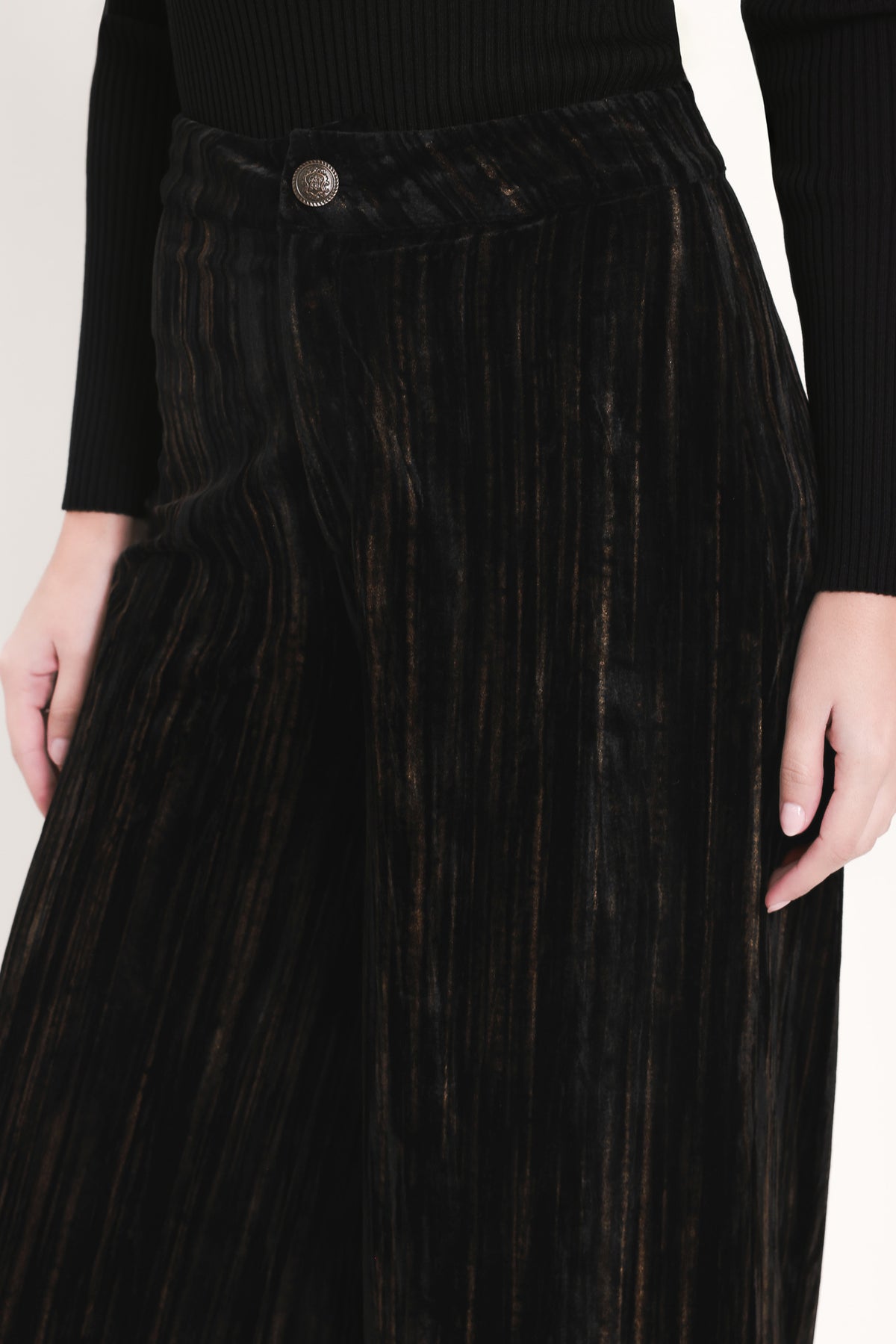 A model wearing high-waisted, wide-leg black pleated velvet trousers with a button waistband | Flying Tomato