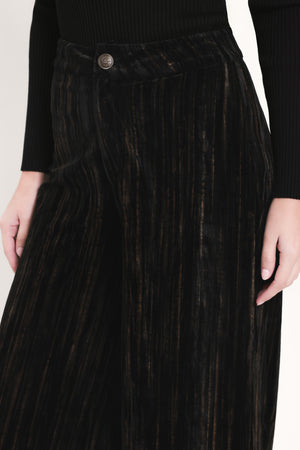 A model wearing high-waisted, wide-leg black pleated velvet trousers with a button waistband | Flying Tomato