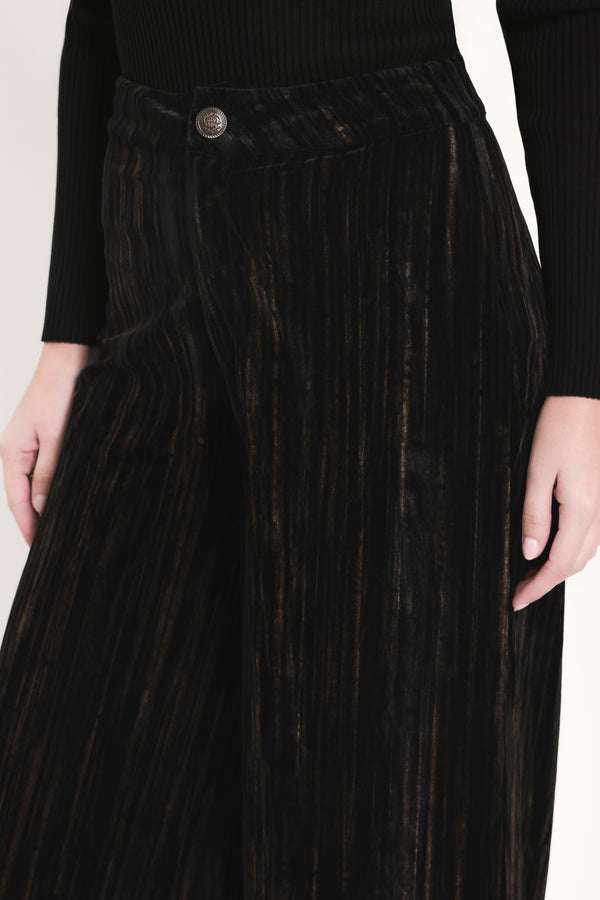 A model wearing high-waisted, wide-leg black pleated velvet trousers with a button waistband | Flying Tomato