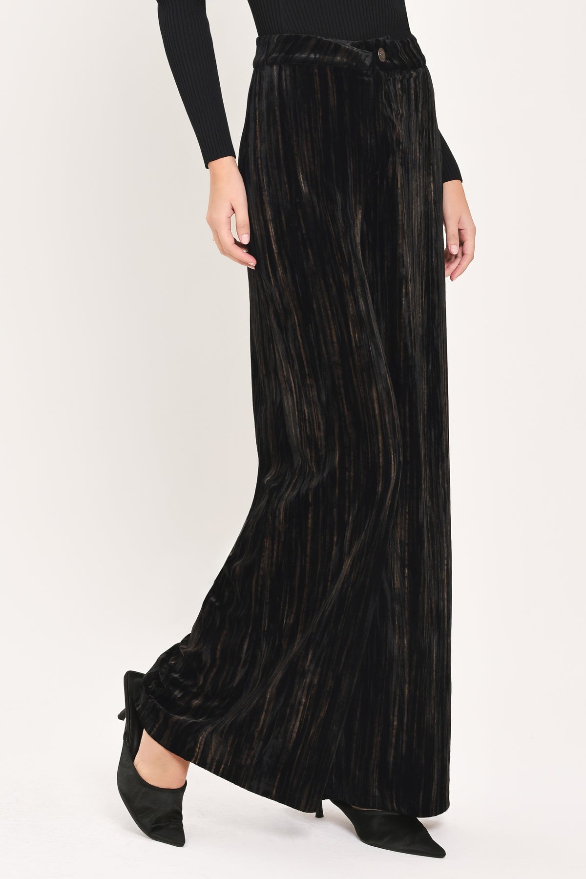 A model wearing high-waisted, wide-leg black pleated velvet trousers with a button waistband | Flying Tomato