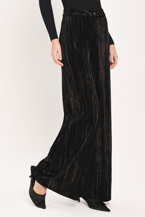 A model wearing high-waisted, wide-leg black pleated velvet trousers with a button waistband | Flying Tomato
