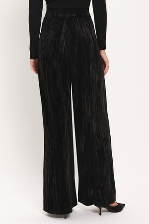 A model wearing high-waisted, wide-leg black pleated velvet trousers with a button waistband | Flying Tomato
