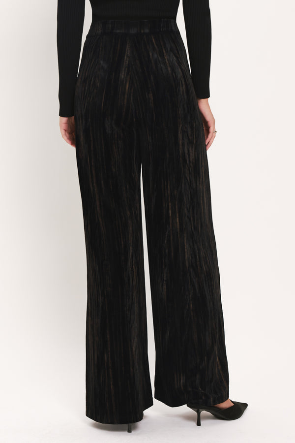 A model wearing high-waisted, wide-leg black pleated velvet trousers with a button waistband | Flying Tomato