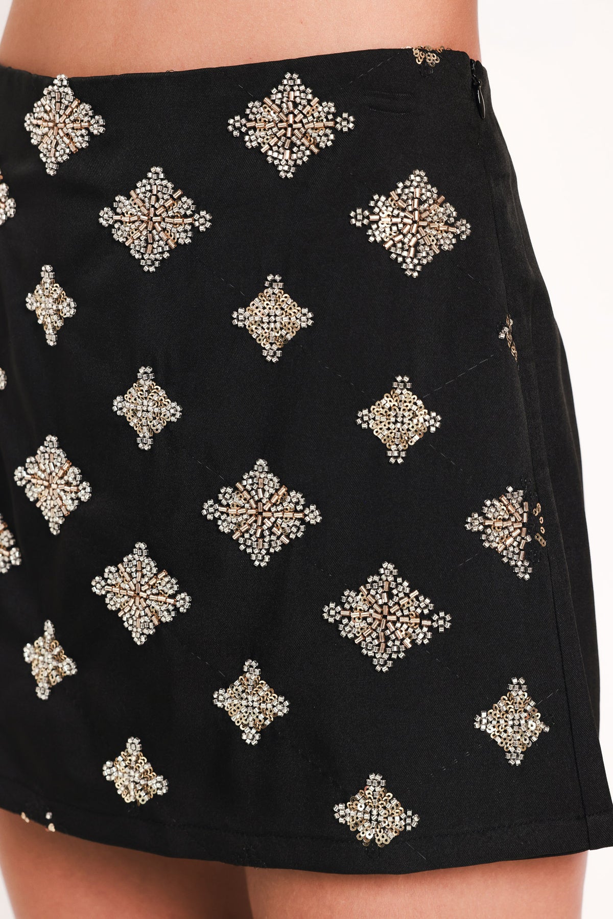 A black A-line mini skort with an allover pattern of metallic gold and silver rhinestone medallions, shown on a model | Flying Tomato