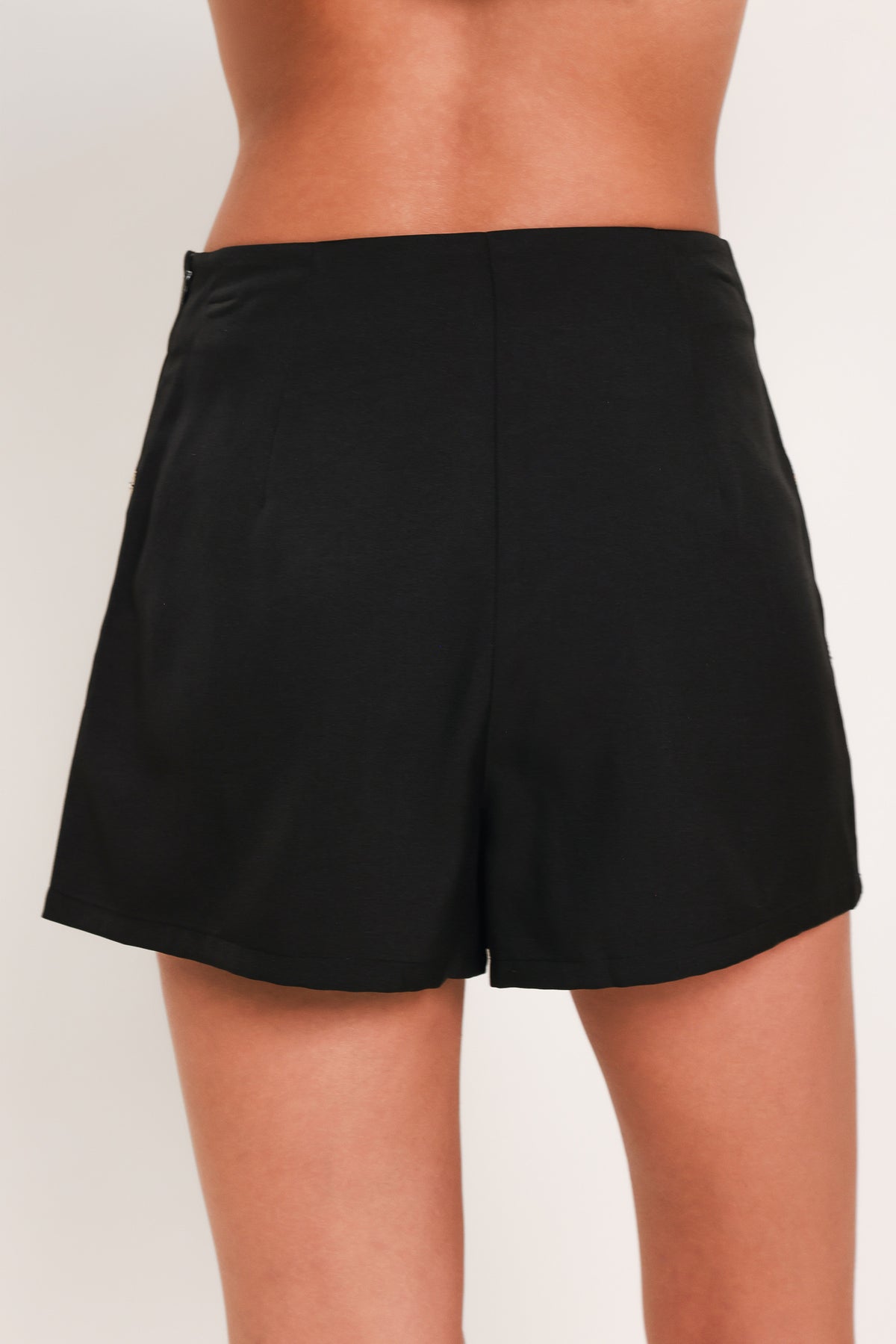A black A-line mini skort with an allover pattern of metallic gold and silver rhinestone medallions, shown on a model | Flying Tomato