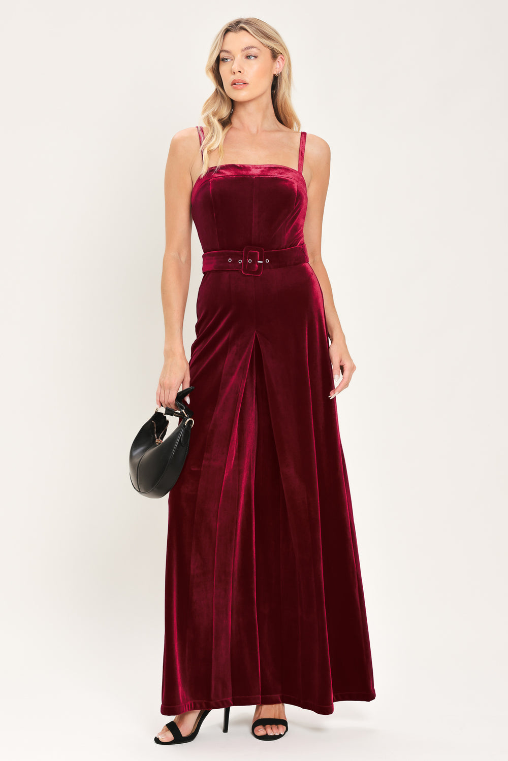 Woman wearing a sleeveless, square-neck red velvet jumpsuit with a matching belt | Flying Tomato
