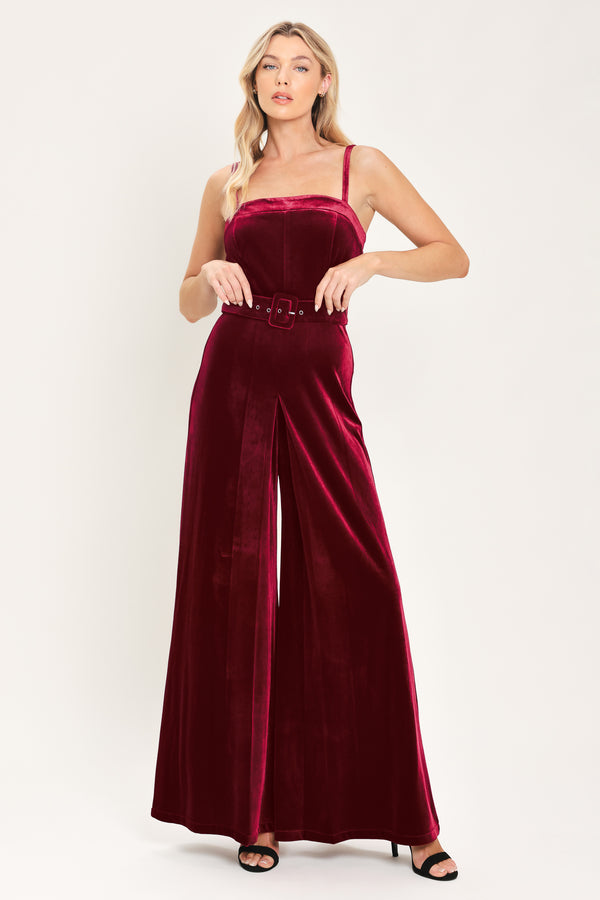 Woman wearing a sleeveless, square-neck red velvet jumpsuit with a matching belt | Flying Tomato