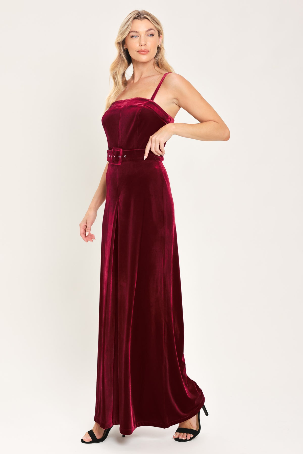 Woman wearing a sleeveless, square-neck red velvet jumpsuit with a matching belt | Flying Tomato