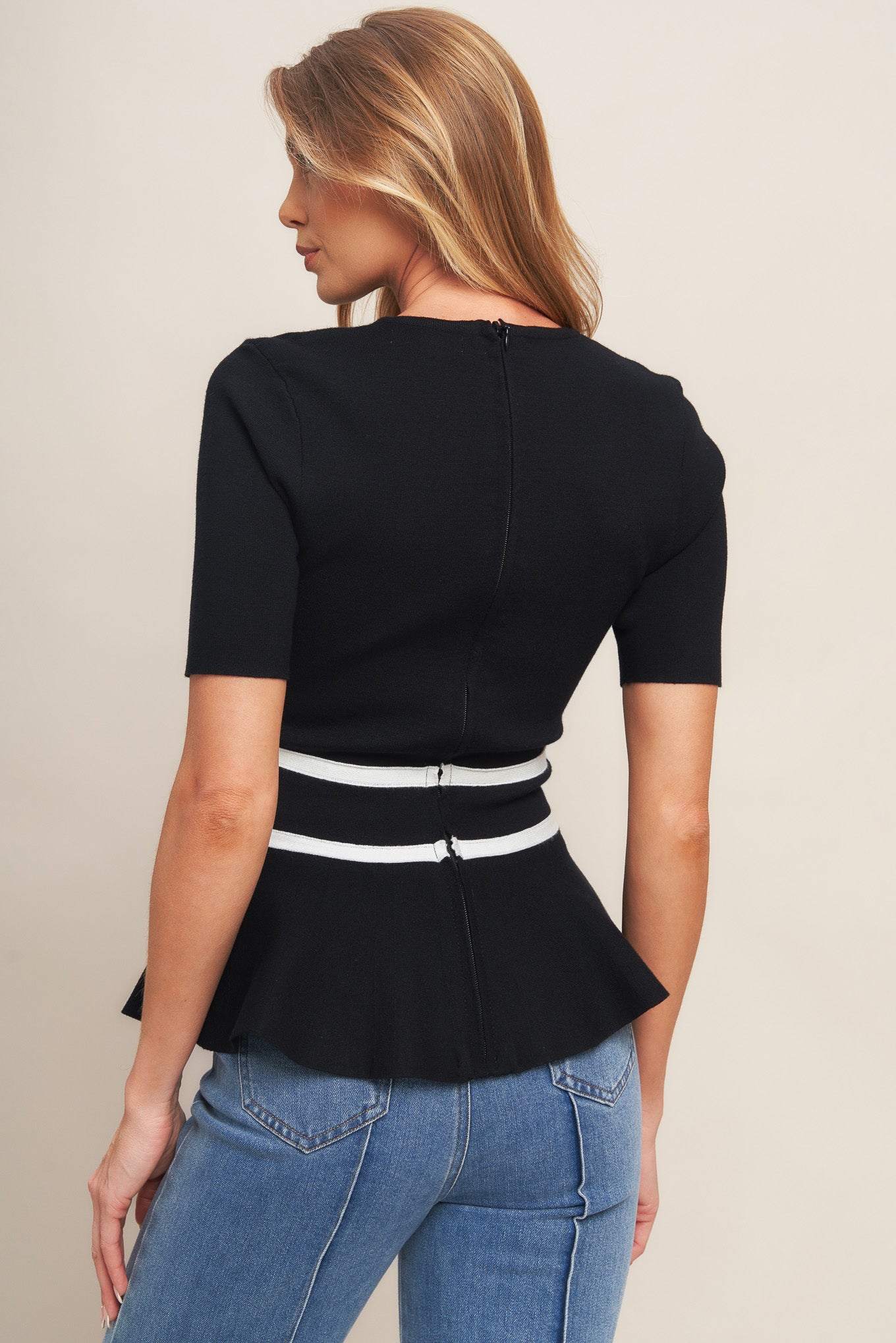A solid sweater knit top featuring round neckline, short sleeve, bow front, peplum and back zipper closure