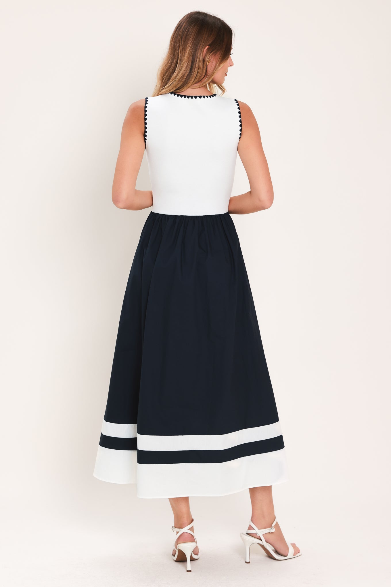 Woman wearing a white and navy blue sweater knit and woven combination midi dress featuring round neckline, sleeveless and full skirt | Flying Tomato