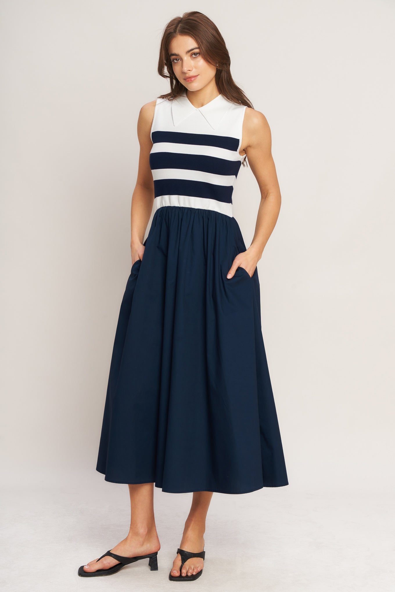 Woman wearing a sleeveless dress with a striped bodice and navy skirt on a white background