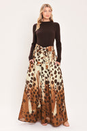 A woman modeling a combination maxi dress with a dark brown mock-neck long-sleeve top paired with a high-waisted, floor-length skirt featuring a brown and cream abstract animal spot pattern with a matching tie belt | Flying Tomato