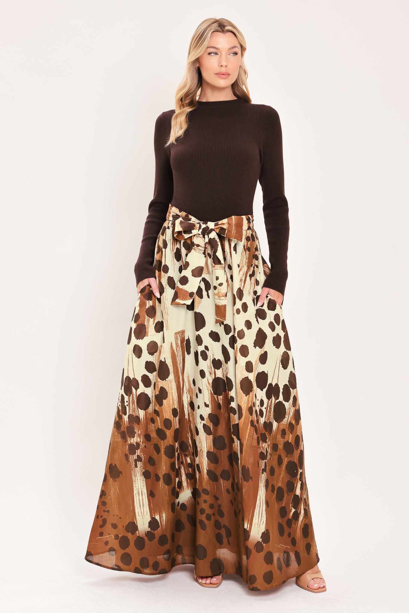 A woman modeling a combination maxi dress with a dark brown mock-neck long-sleeve top paired with a high-waisted, floor-length skirt featuring a brown and cream abstract animal spot pattern with a matching tie belt | Flying Tomato