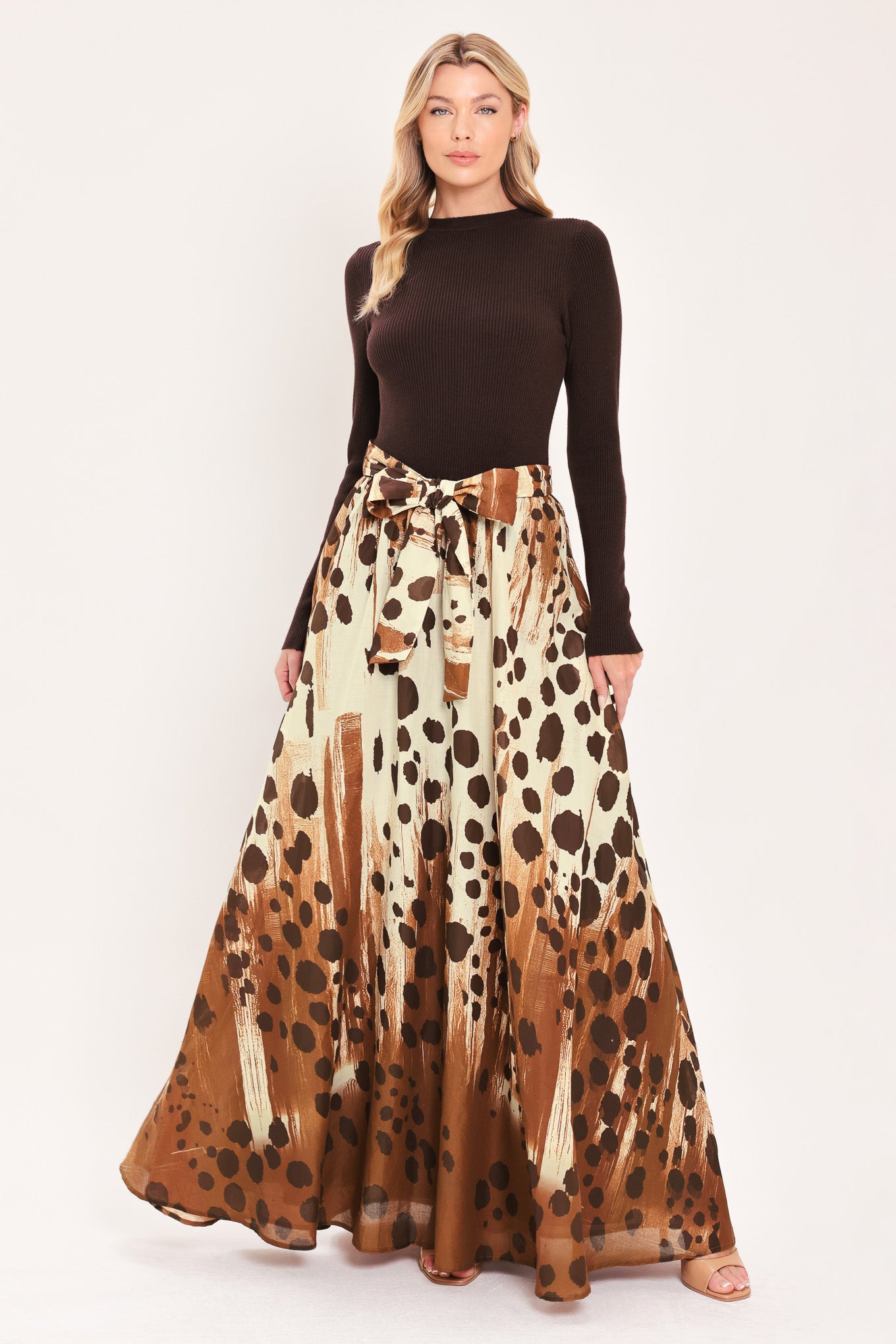 A woman modeling a combination maxi dress with a dark brown mock-neck long-sleeve top paired with a high-waisted, floor-length skirt featuring a brown and cream abstract animal spot pattern with a matching tie belt | Flying Tomato