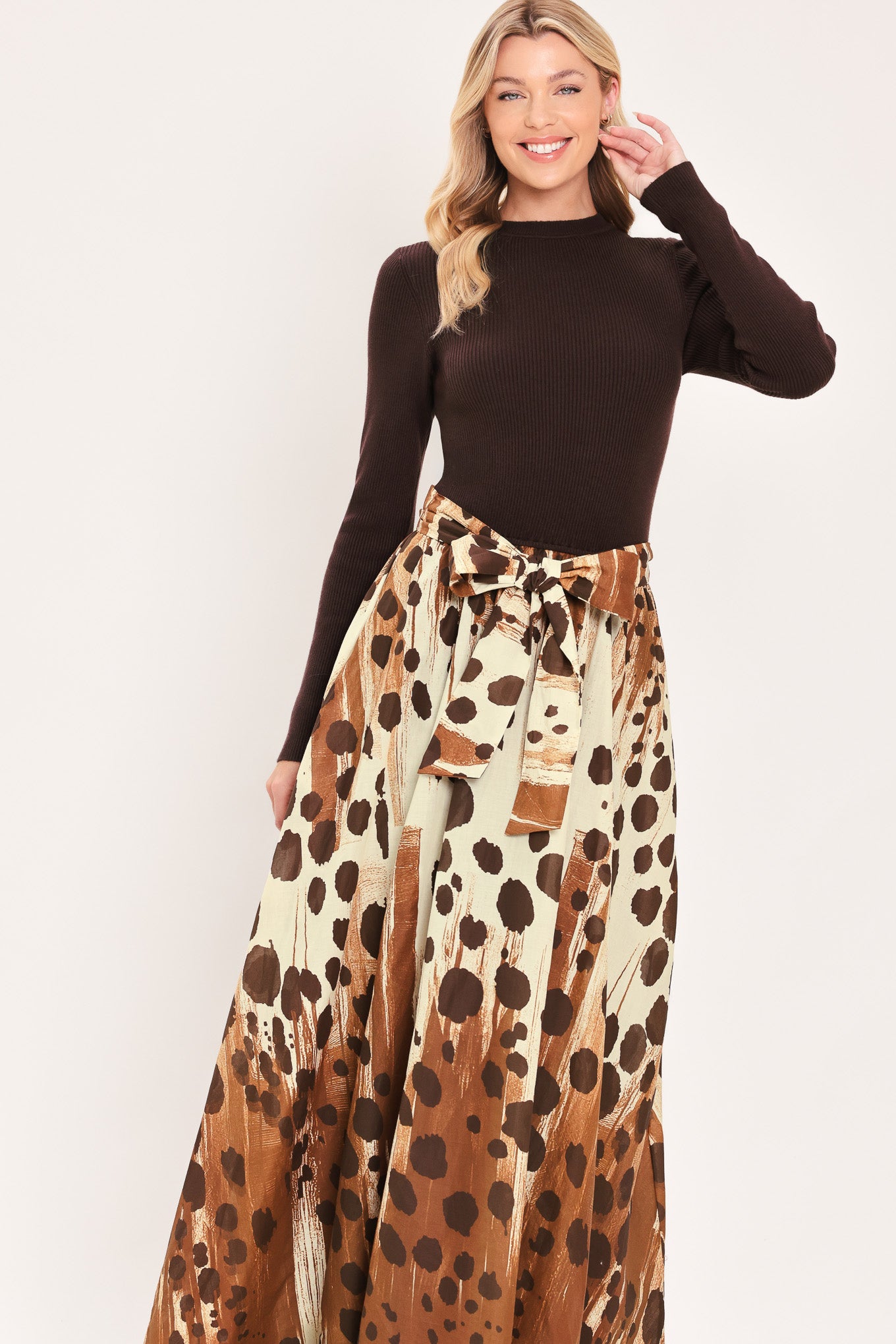 A woman modeling a combination maxi dress with a dark brown mock-neck long-sleeve top paired with a high-waisted, floor-length skirt featuring a brown and cream abstract animal spot pattern with a matching tie belt | Flying Tomato