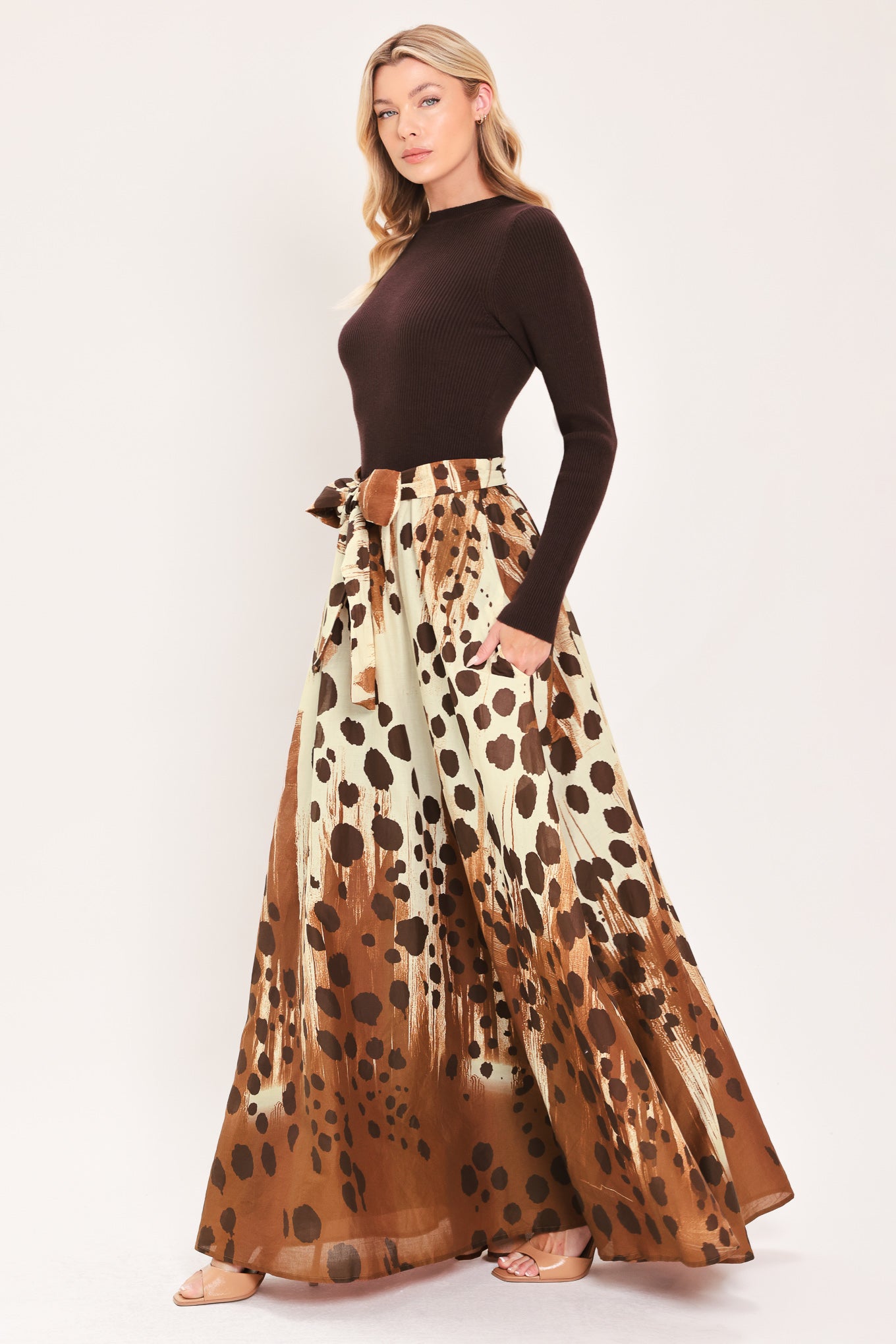 A woman modeling a combination maxi dress with a dark brown mock-neck long-sleeve top paired with a high-waisted, floor-length skirt featuring a brown and cream abstract animal spot pattern with a matching tie belt | Flying Tomato