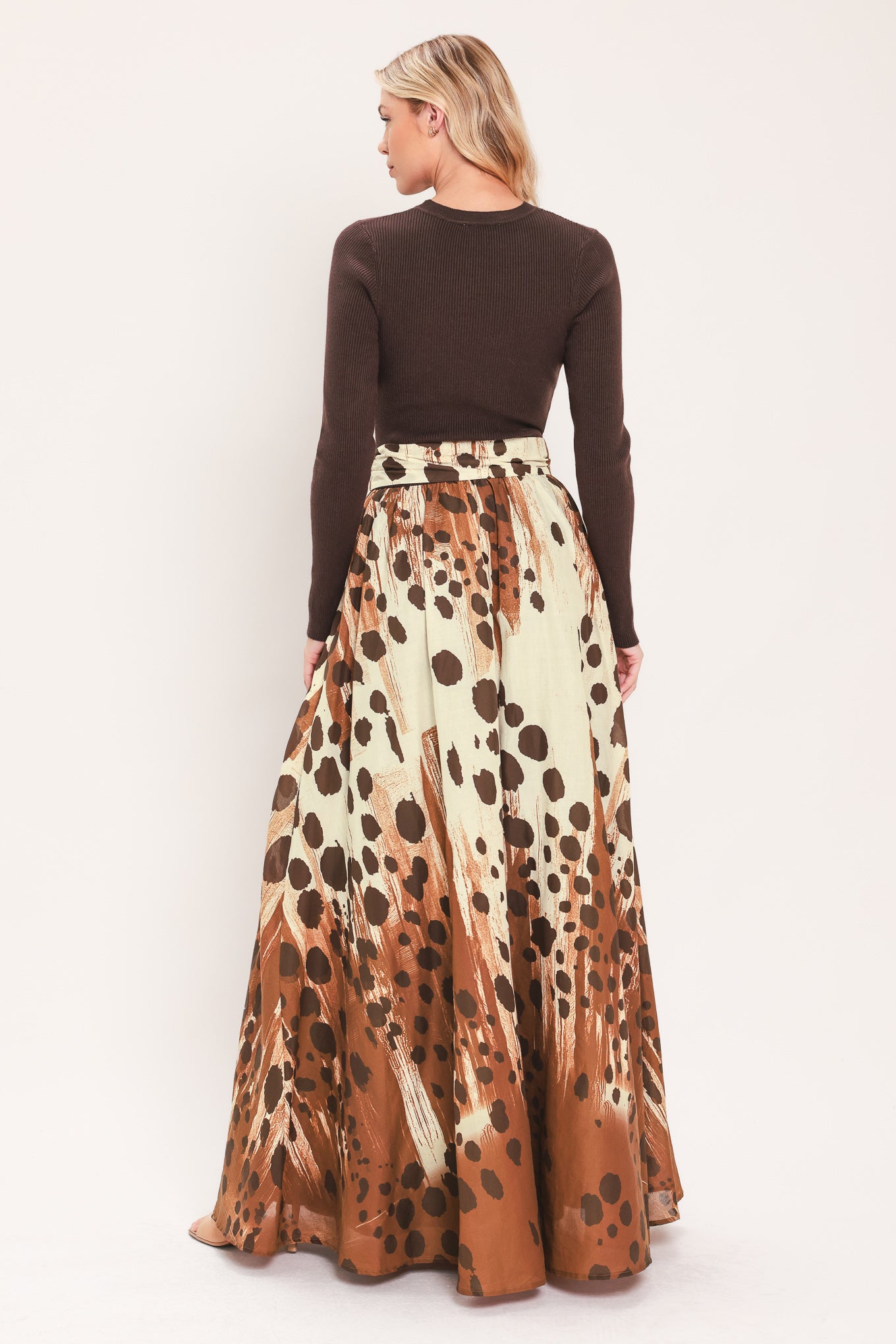 A woman modeling a combination maxi dress with a dark brown mock-neck long-sleeve top paired with a high-waisted, floor-length skirt featuring a brown and cream abstract animal spot pattern with a matching tie belt | Flying Tomato