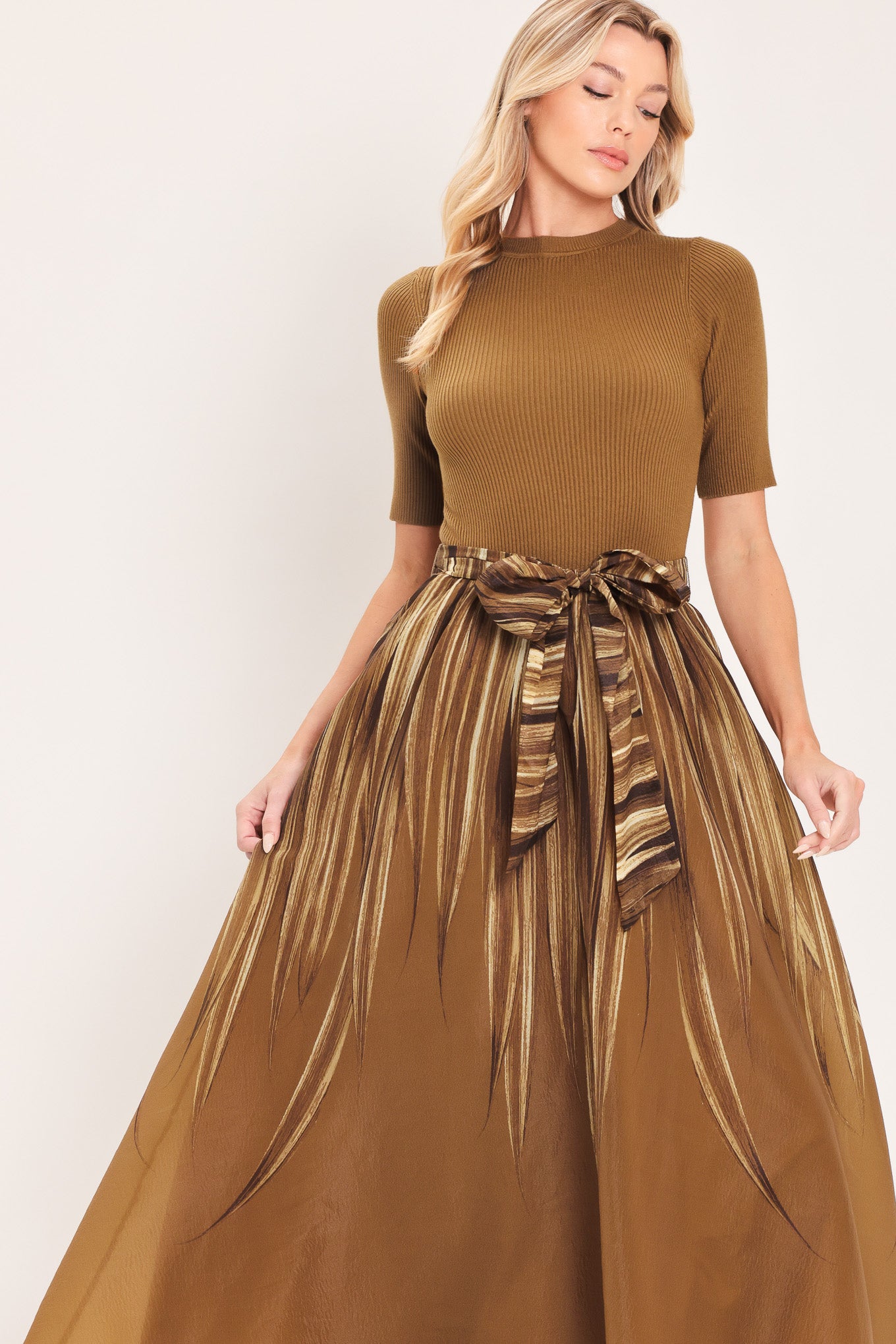 A woman modeling a brown midi dress with a short-sleeve mock neck top, pleated skirt, and a matching fabric tie belt | Flying Tomato