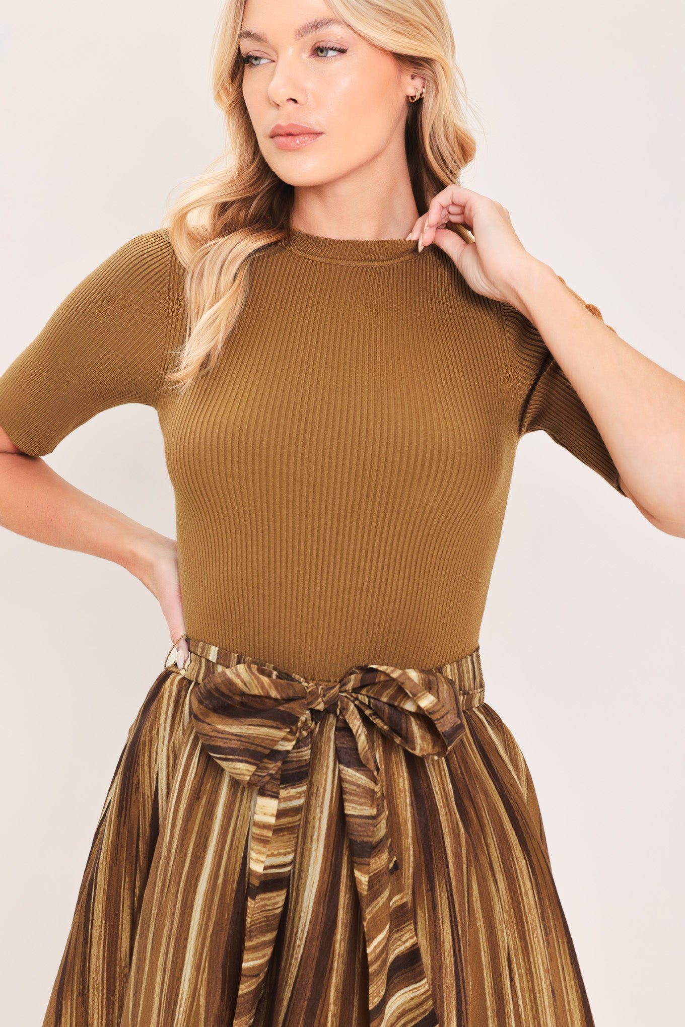 A woman modeling a brown midi dress with a short-sleeve mock neck top, pleated skirt, and a matching fabric tie belt | Flying Tomato